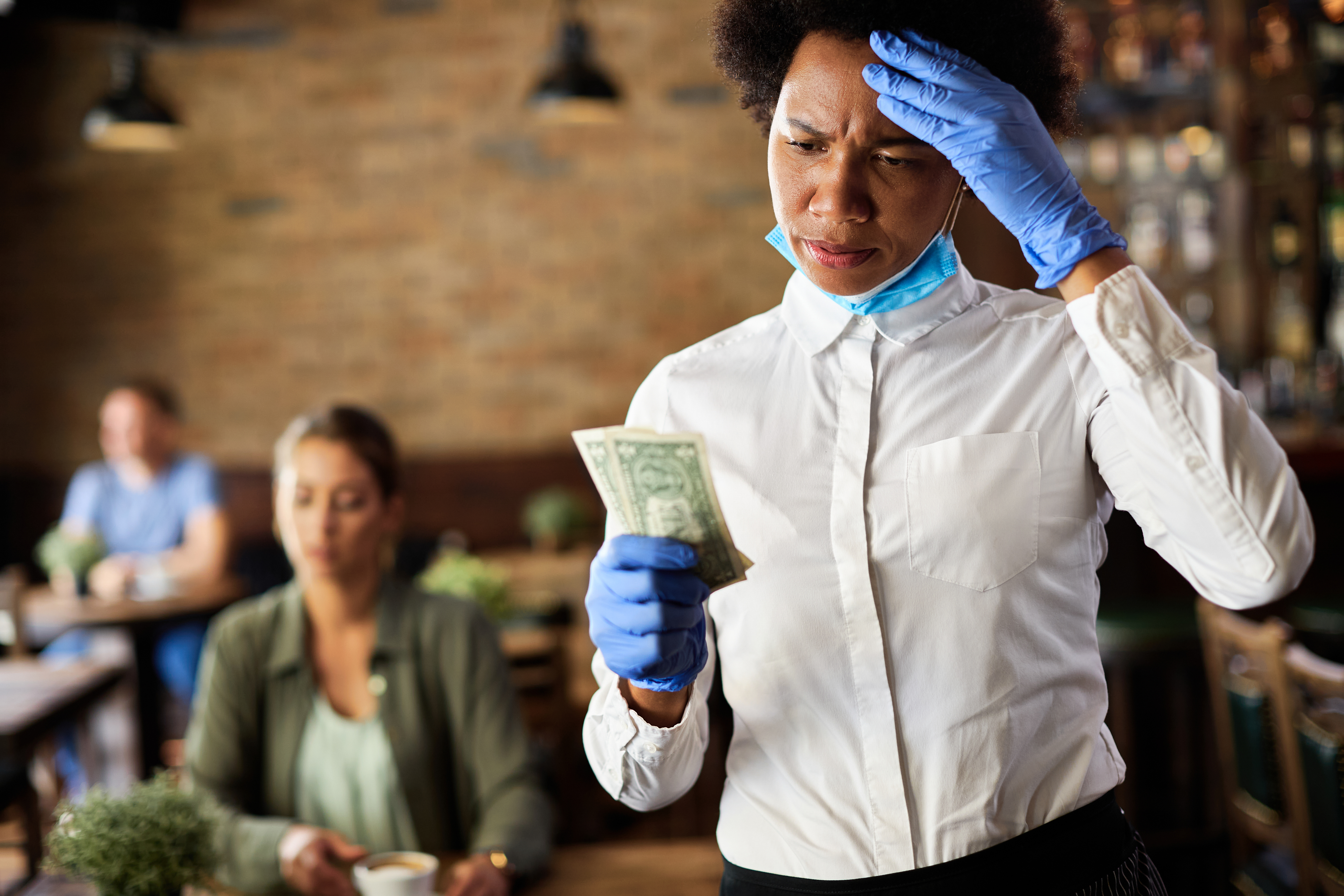 Displeased black waitress feeling disappointed with tip she has received from a customer in a pub.
